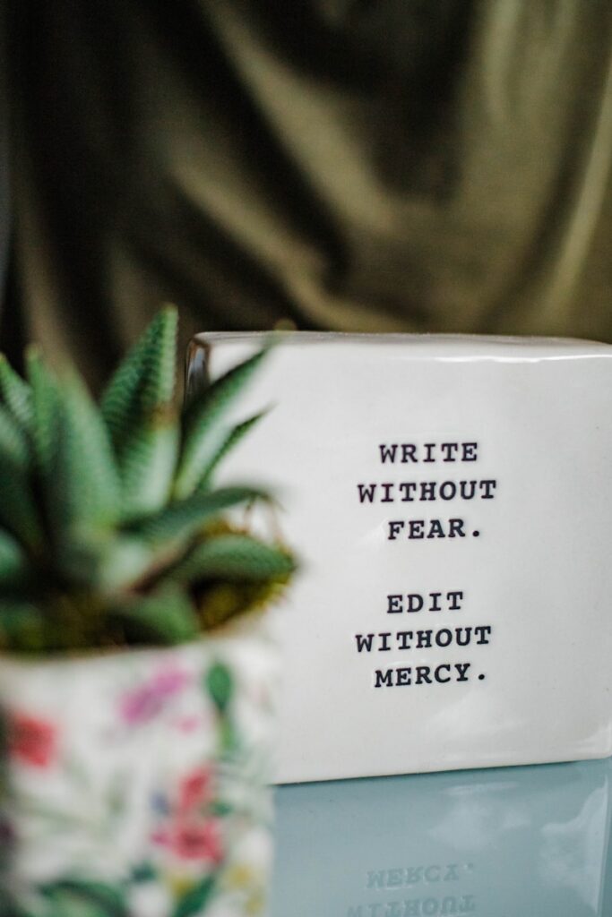 a white box with writing 'write without fear, edit without mercy' next to a plant
